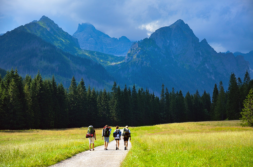 Hikers walking down a path leading to towering mountains