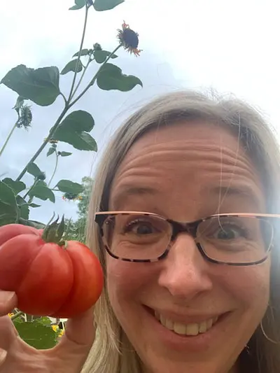 Kris Skavish, holding a ripe tomato, with a sunflower in the background.